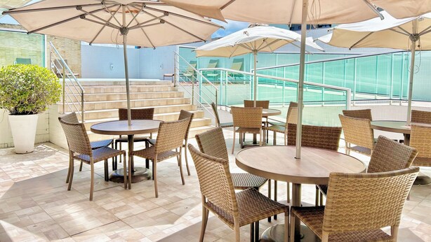 Terraza con mesas redondas y sillas de mimbre, todo bajo grandes sombrillas.