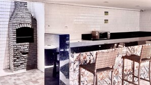 Una cocina con horno de ladrillo integrado, microondas y una barra con azulejos estampados y taburetes de mimbre.