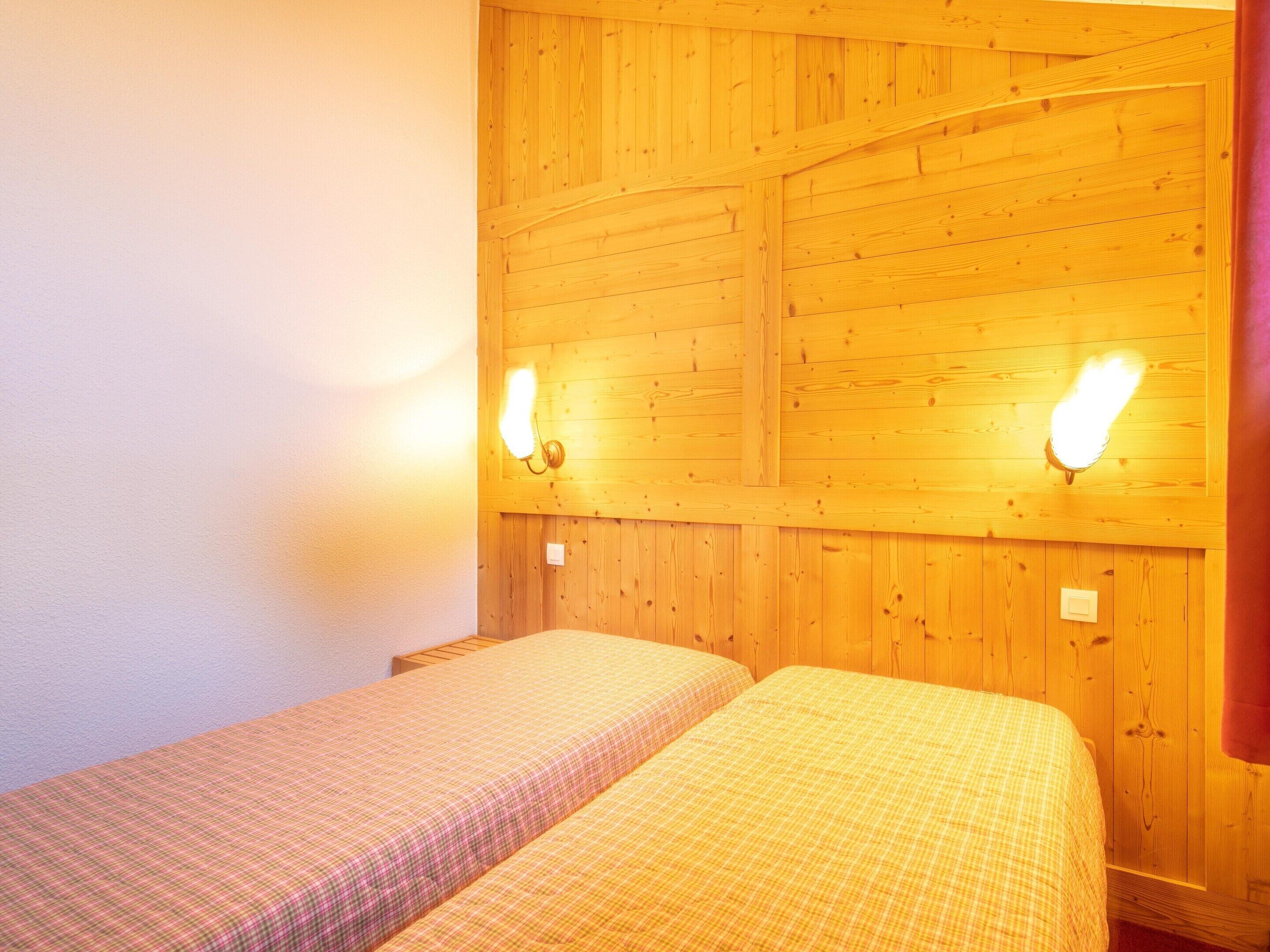 A room with two beds, wooden panel walls, and wall-mounted lights.