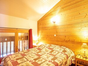Ein gemütliches Zimmer mit Holzbalkendecke, einem Bett mit geblümter Steppdecke, einem Nachttisch mit Lampe und einer Schiebetür mit rotem Vorhang.