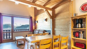 En inredning med träpanel, ett matbord, stolar, en bänk, en plats för att göra kaffe och en utsikt över bergen genom stora fönster.