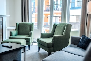 Ein modernes Hotelzimmer mit zwei grünen Sesseln, einem grauen Sofa und einem kleinen Tisch.