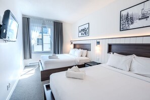 A hotel room with two beds, a television, a window with curtains, and a framed picture on the wall.