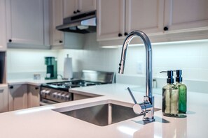 Eine moderne Küche mit einem Edelstahl-Spülbecken, einem Wasserhahn und zwei Seifenspendern auf der Arbeitsfläche.