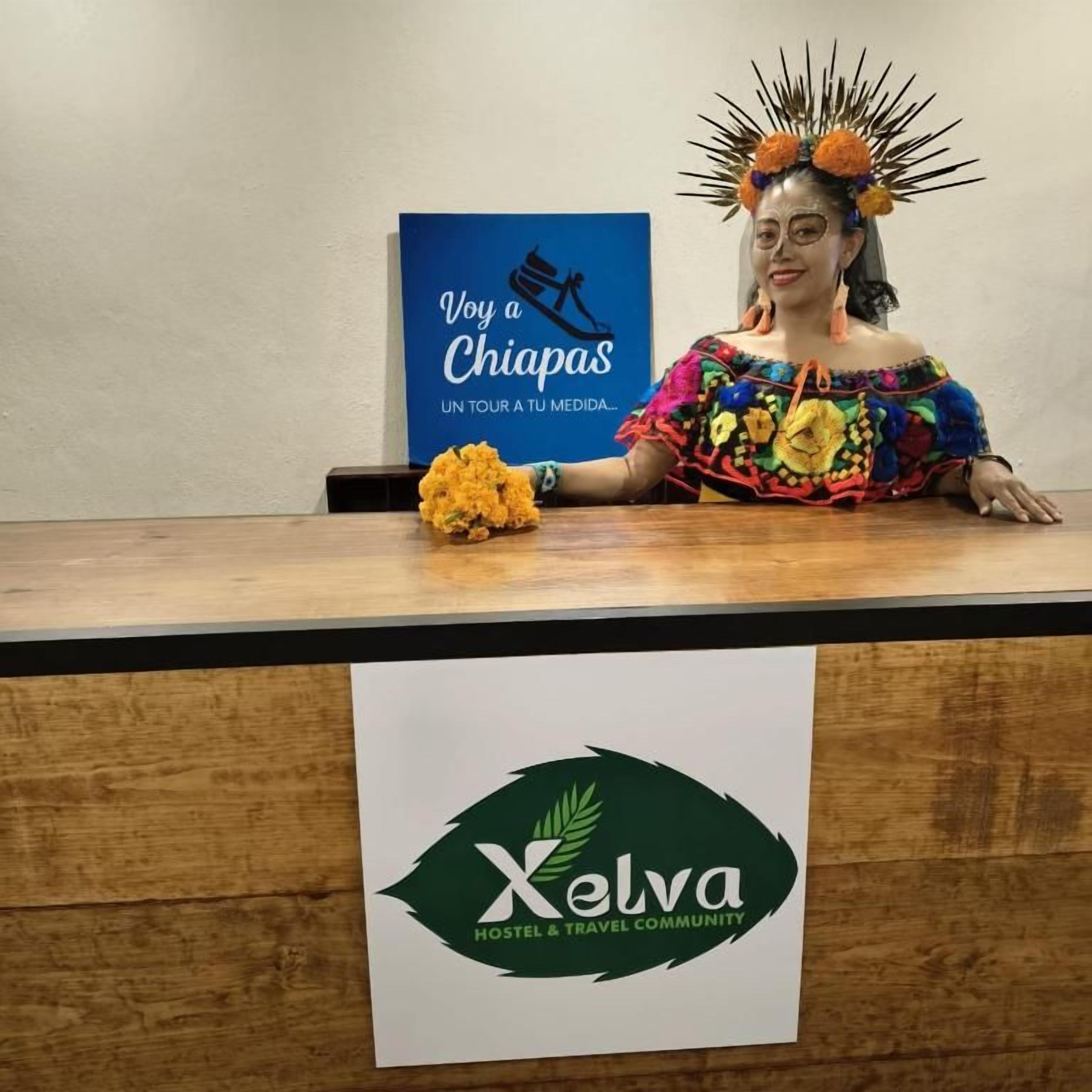 Una persona seduta a una scrivania di legno con un cartello che recita 'Xelva Hostel & Travel Community'.