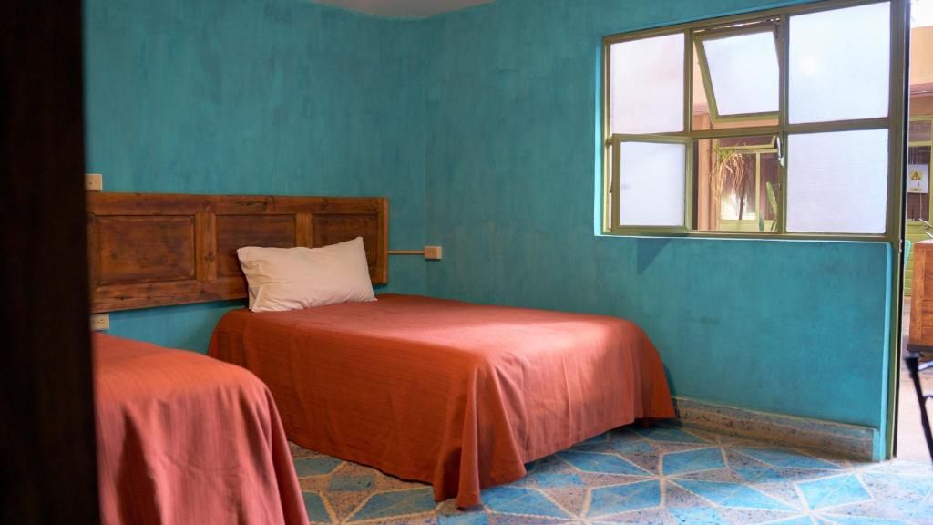 Une chambre avec deux lits, une fenêtre avec des stores et un sol à motifs bleus.
