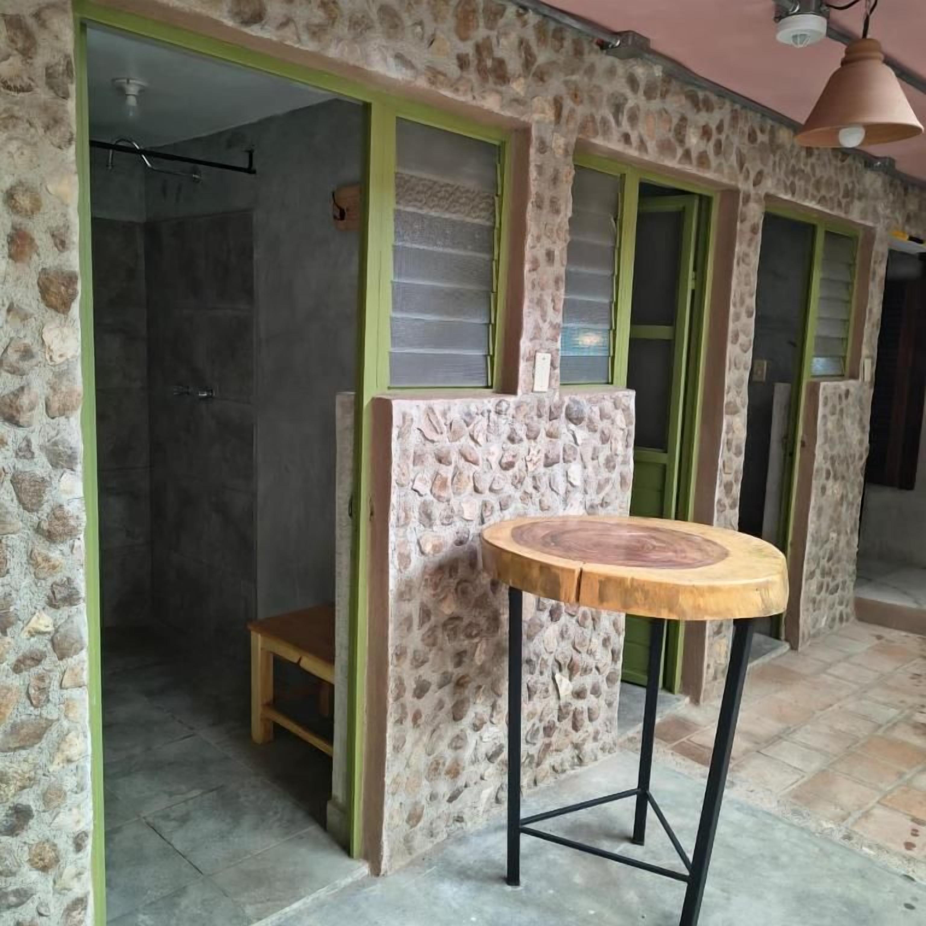 Une pièce avec un mur en pierre, un tabouret en bois et un espace douche.