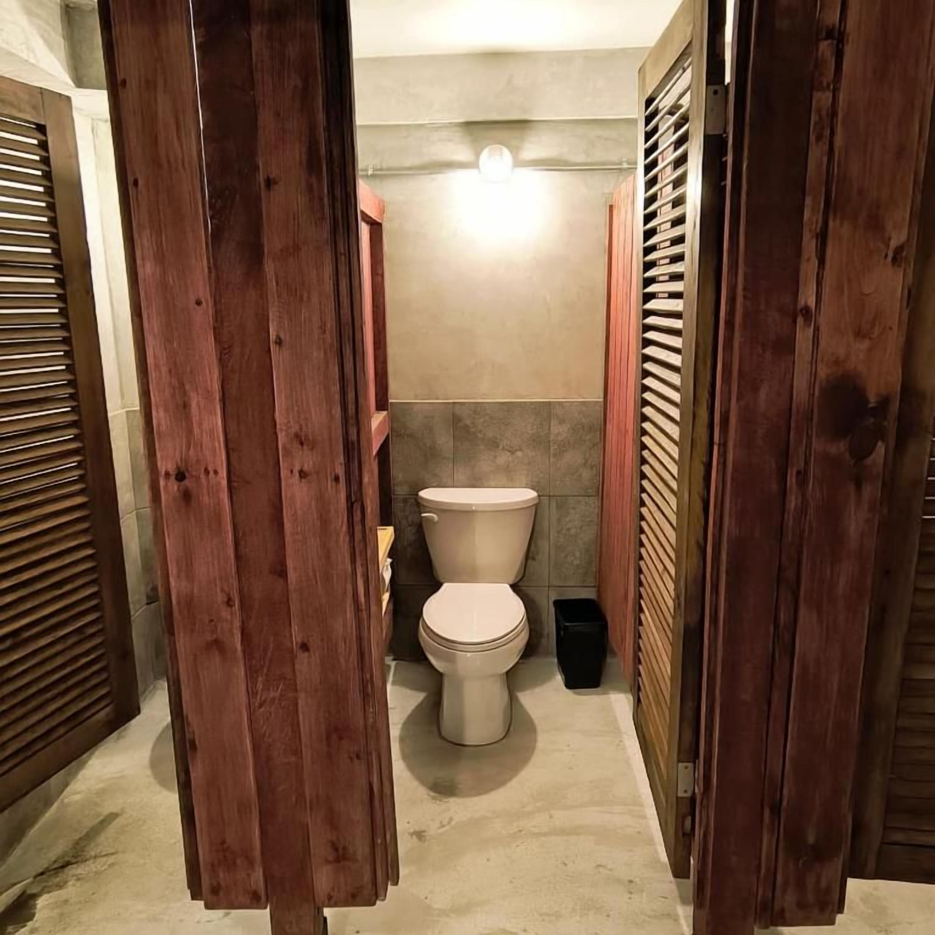 Une petite salle de bain avec des toilettes, une poubelle et des portes en bois.