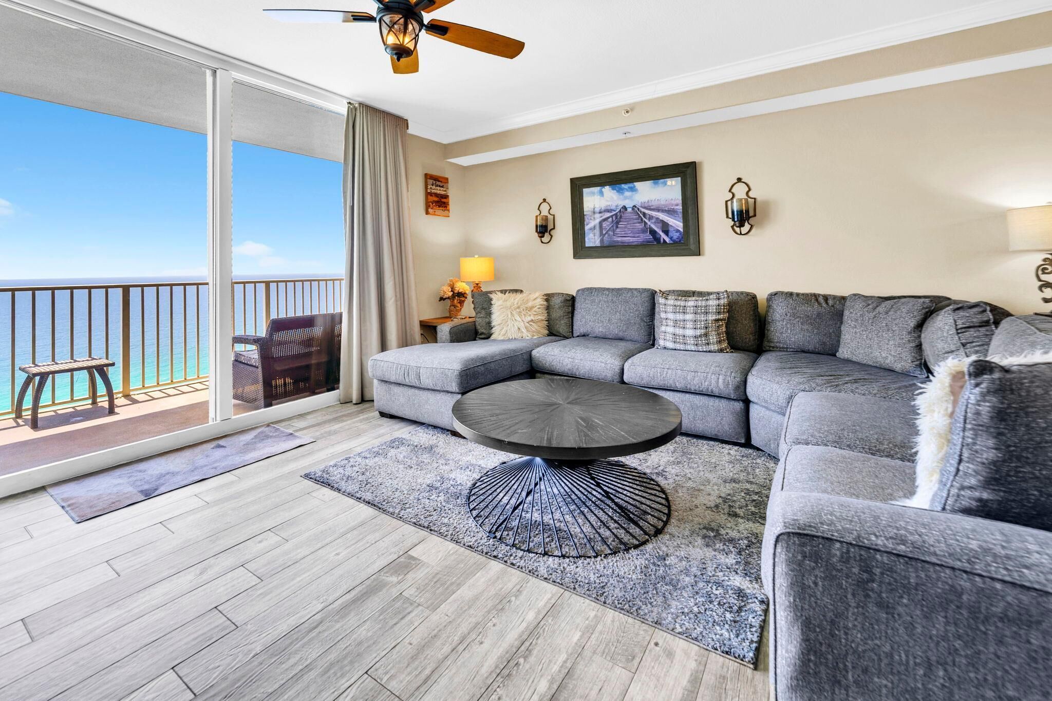 A modern living room with a gray sectional sofa, a round coffee table, and a view of the ocean through a sliding glass door.