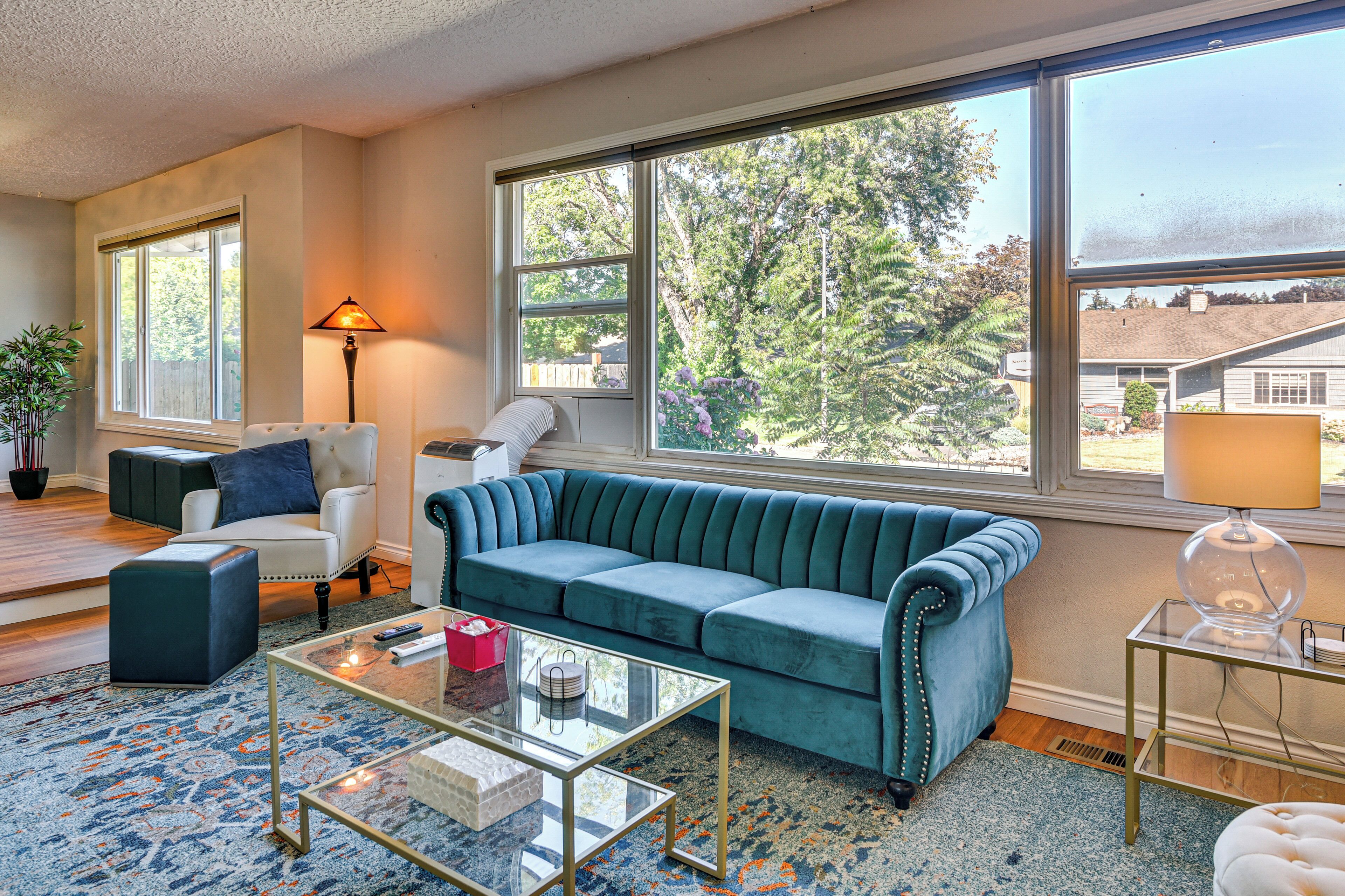 A living room with a blue sofa, a white armchair, a glass coffee table, and a lamp.