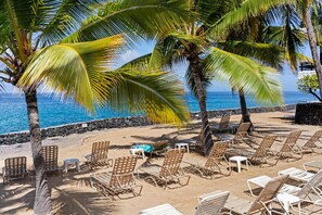 Ein Strand mit Liegestuhlreihen und Palmen, eine felsige Küstenlinie und ein klares, blaues Meer.