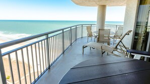 A balcony with a view of the ocean, a table, and chairs.