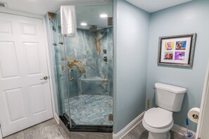 Un baño con ducha envuelta en cristal, inodoro blanco y un cuadro en la pared.