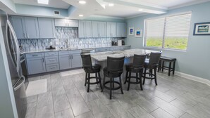 A kitchen with light blue cabinets, a marble island, and bar stools.