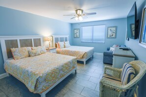 Un dormitorio con dos camas, un escritorio, una silla, un ventilador de techo y obras de arte en las paredes.