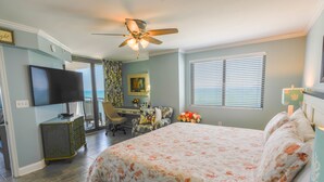 A bedroom with a bed, a desk, a chair, a television, and a ceiling fan.