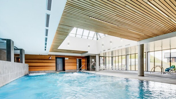 An indoor swimming pool with a wooden ceiling, clear glass walls, and a view of the outdoors. - High-altitude Home for 4 (Garin)