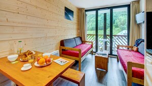 A wooden cabin with a dining table set with breakfast, two single beds, a sofa, and a TV. - High-altitude Home for 4 (Garin)