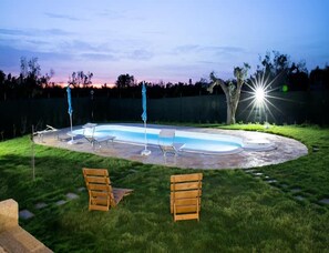 A backyard with a swimming pool, two wooden chairs, and a patio umbrella. - Prestige Pool Trullo (Racale)