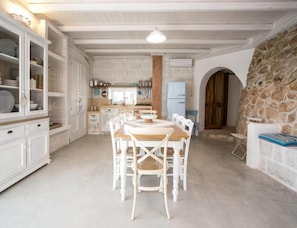 A spacious kitchen with white cabinetry, a dining table with chairs, and a stone wall. - Prestige Pool Trullo (Racale)