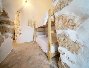A rustic stone-walled room with a bunk bed and a single bed, a wall-mounted light fixture, and a stone floor. - Prestige Pool Trullo (Racale)