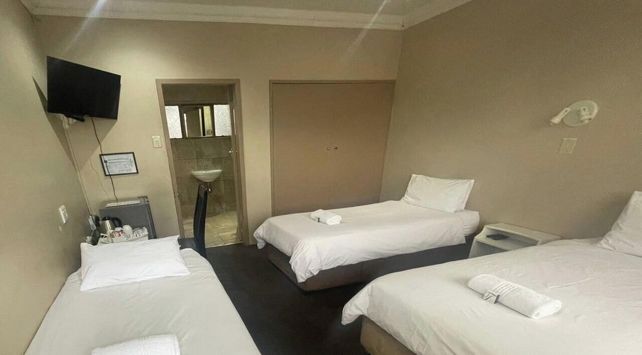 A hotel room with two beds, a TV, a sink, and a door leading to a bathroom.