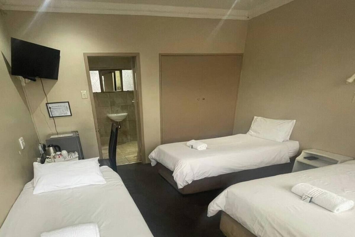 A hotel room with two beds, a TV, a sink, and a door leading to a bathroom.