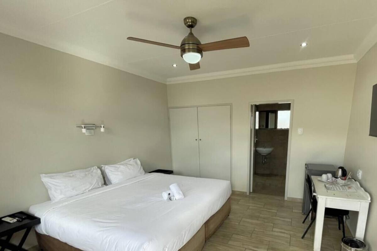 A hotel room with a bed, a desk, a ceiling fan, a TV, and a bathroom visible through an open door.