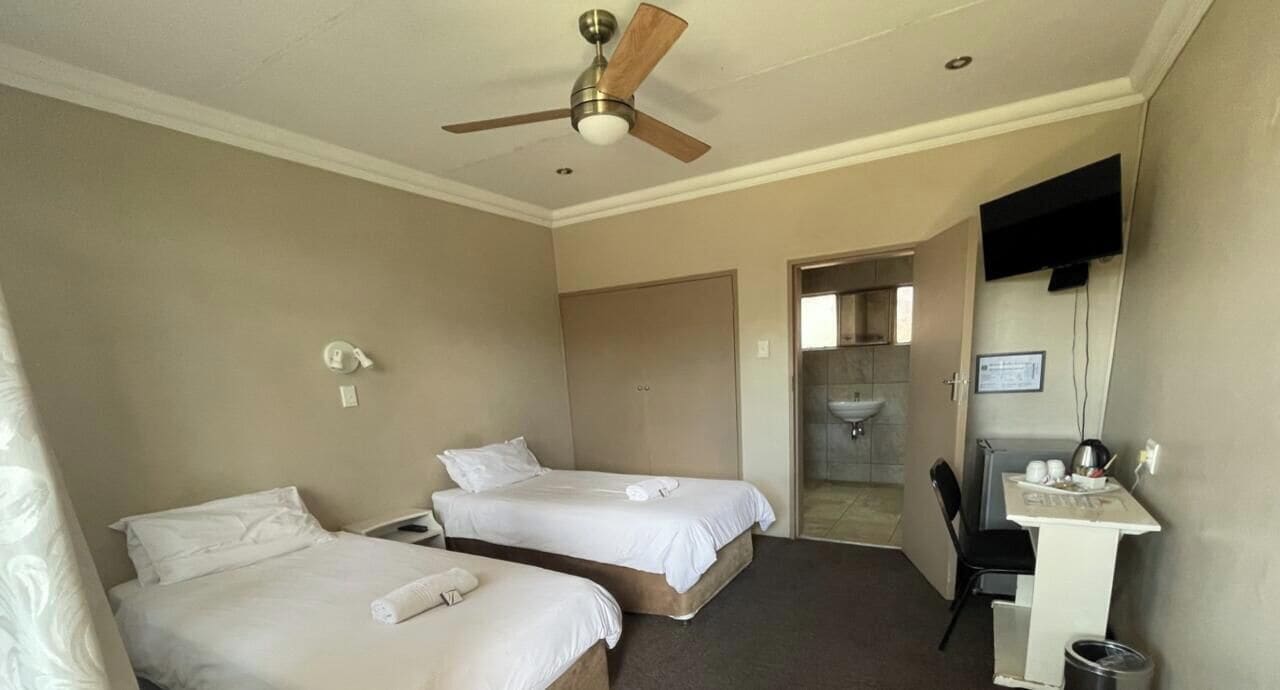 A hotel room with two beds, a ceiling fan, a desk with a chair, and a TV mounted on the wall.