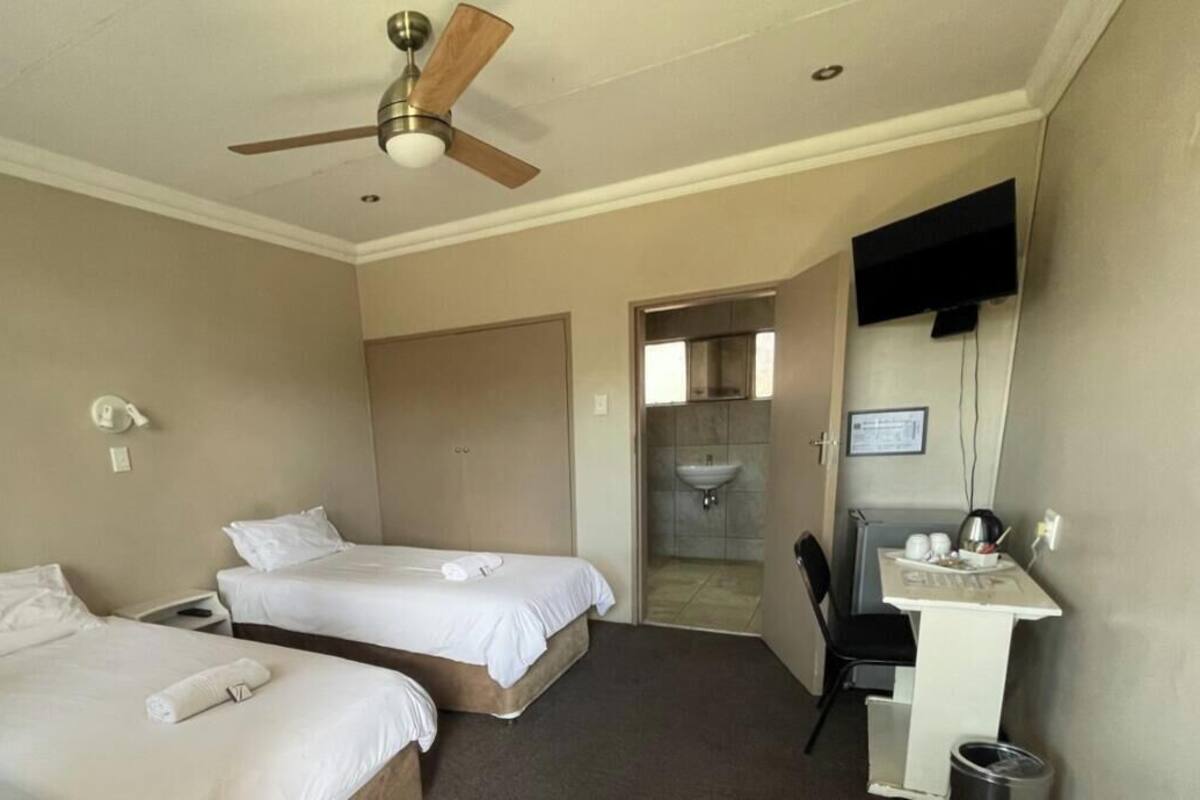 A hotel room with two beds, a ceiling fan, a desk with a chair, and a TV mounted on the wall.