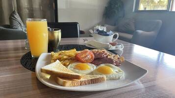 Une assiette de petit-déjeuner avec des œufs, du bacon, des tomates et des toasts, un verre de jus d’orange et une tasse de café, le tout posé sur une table.