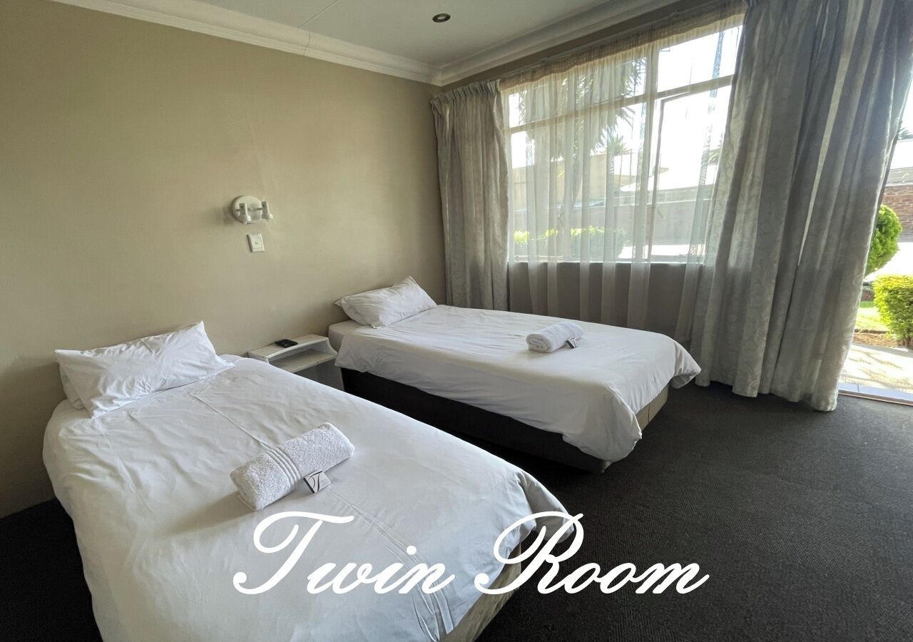 A twin room with two beds, a window with curtains, and a wall-mounted light fixture.