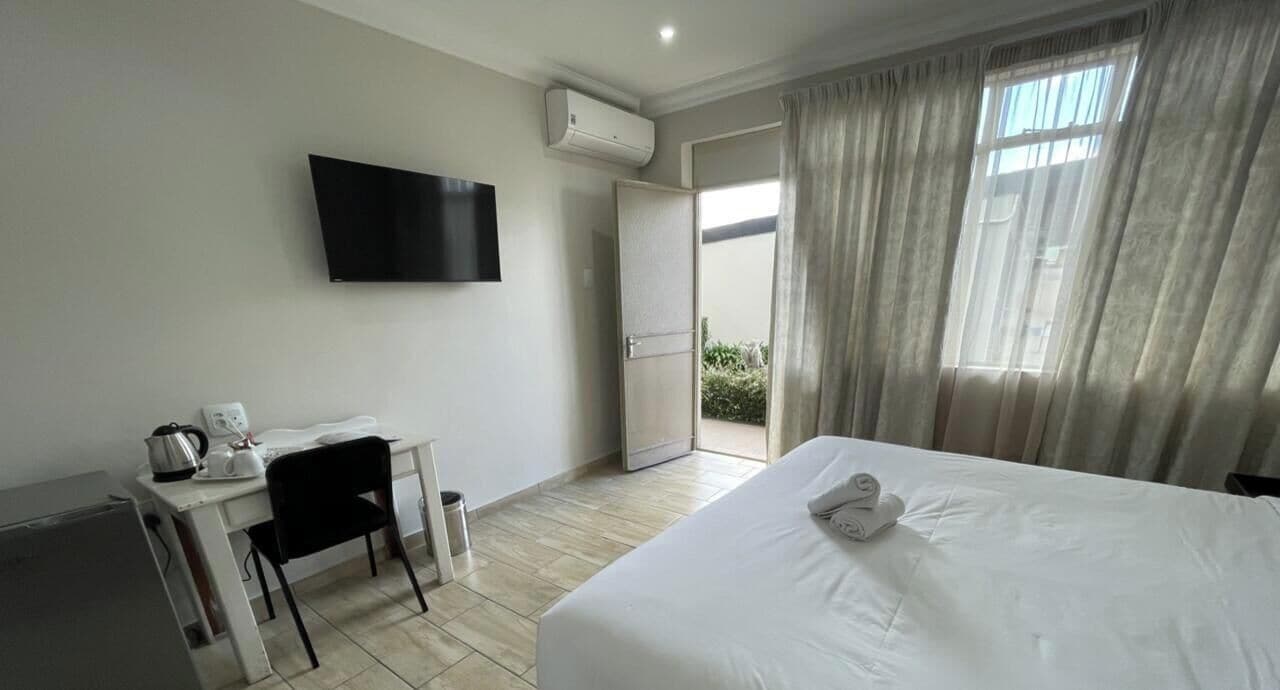 A hotel room with a bed, a desk with a chair, a television, and a sliding door to the outside.