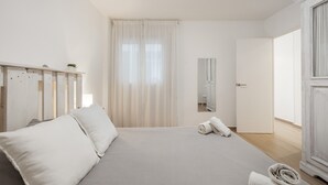 Een minimalistische slaapkamer met een bed, een spiegel, een kledingkast en een raam met gordijnen.