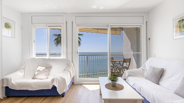 Een moderne woonkamer met een bank, een stoel, een salontafel en uitzicht op zee door grote schuifdeuren.