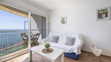 A balcony with a view of the sea, a white sofa, a small table with a plant, and a chair.