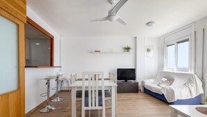 Een moderne woonkamer met een eethoek, een bank, een televisie en een plafondventilator.