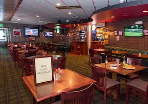 A restaurant with multiple seating areas, including booths and tables. There are televisions mounted on the walls, a bar area, and a sign indicating free daily breakfast. - Comfy Hotel Stay w/ Work Desk & Breakfast | Nr MFR (Medford)