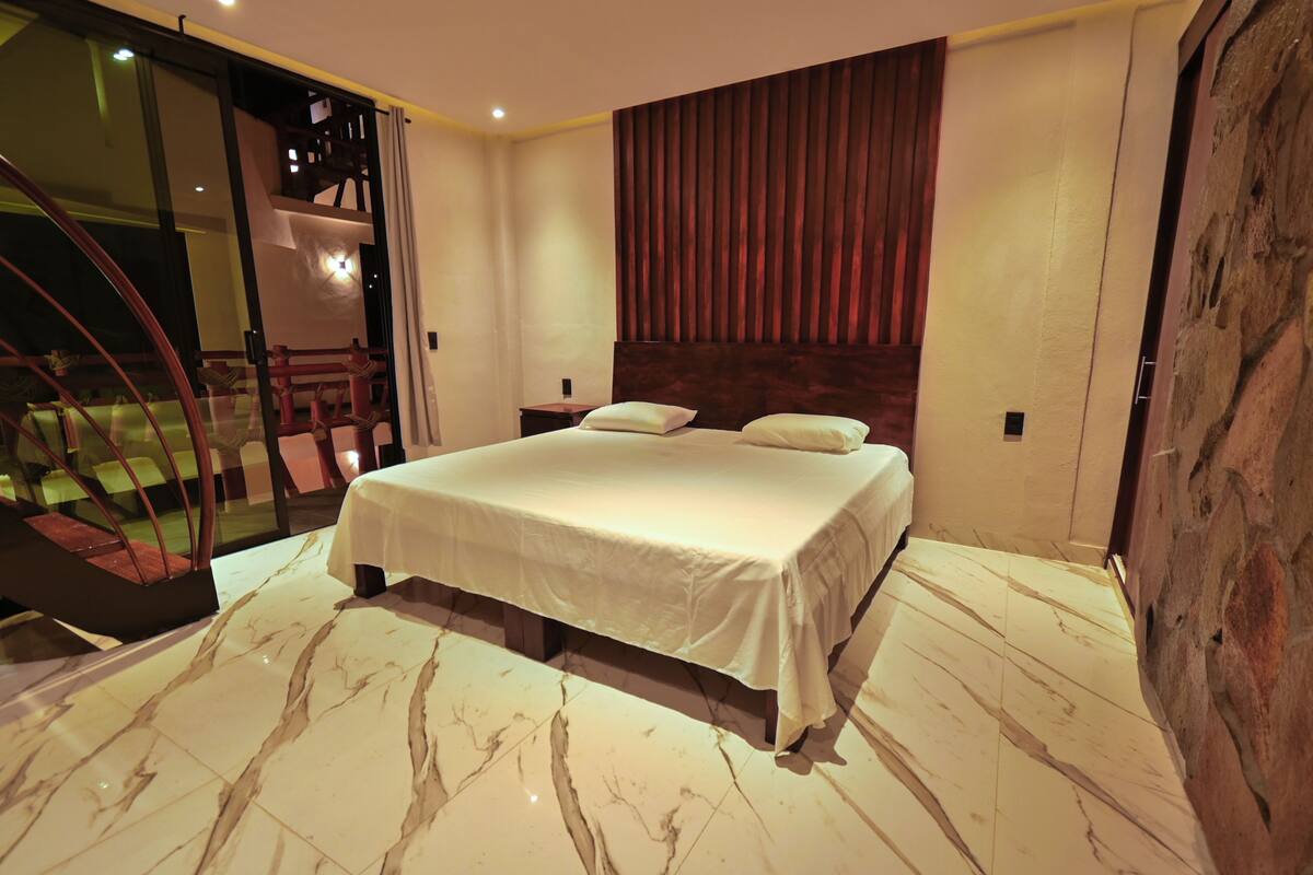 A bedroom with a large bed, a wooden headboard, a marble floor, a nightstand, and a staircase.