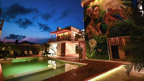 Un área de piscina con un mural, un edificio con balcón y cielo despejado.
