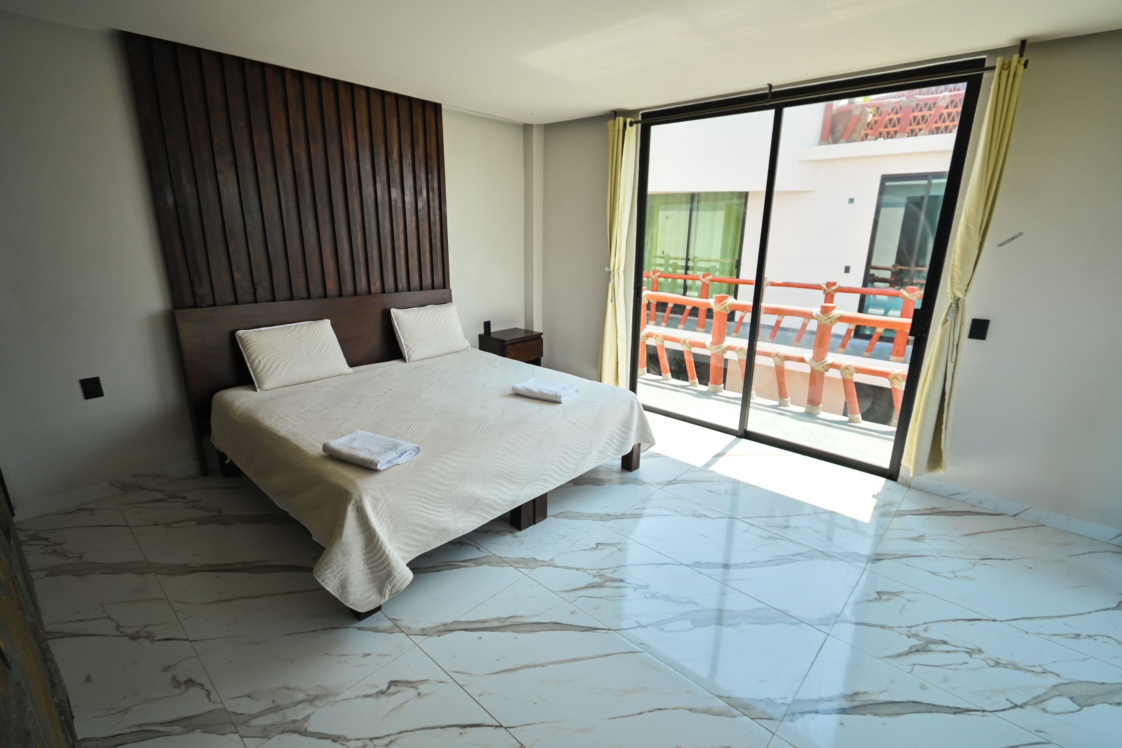 A hotel room with a bed, a nightstand, a large window, and a view of a balcony.