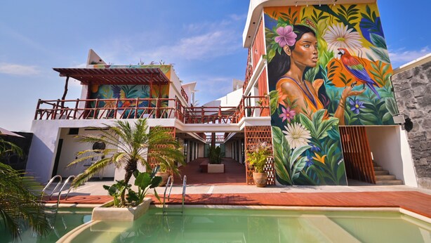 Un hotel moderno con piscina, un mural tropical y una estructura de dos pisos.