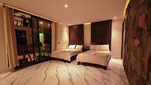 Habitación de hotel con dos camas, puerta de vidrio que da a un balcón, piso de mármol y una pared de acento de piedra.