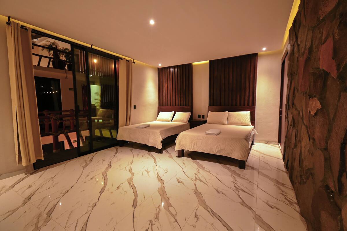 A hotel room with two beds, a glass door leading to a balcony, marble flooring, and a stone accent wall.