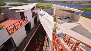 Un hotel moderno con terraza en la azotea y vistas a un cuerpo de agua, que cuenta con piscina y sillones de descanso.