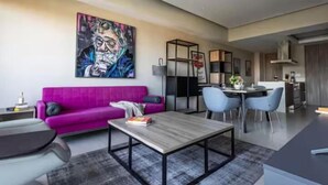 A modern living room with a vibrant pink sofa, a coffee table, and a dining area with blue chairs. - Parklife Pabellon (Guadalajara)