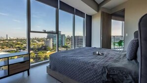 A bedroom with a large bed, a desk, and a view of a cityscape through large windows. - Parklife Pabellon (Guadalajara)