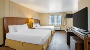 A hotel room with two beds, a desk, a TV, and a window with curtains.