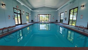An indoor swimming pool with clear glass walls, safety signs, and a view of greenery outside.
