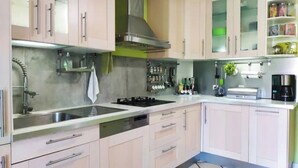 Een keuken met lichte kastjes, roestvrijstalen apparatuur en een betegelde vloer.
